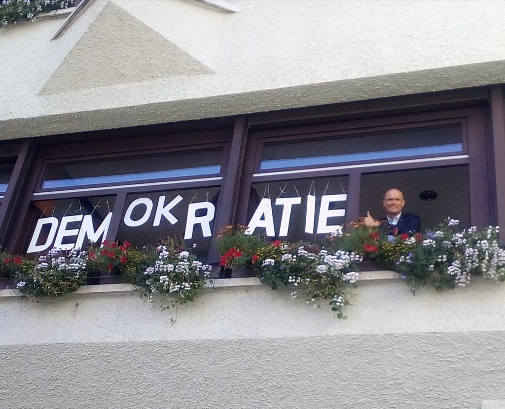 Der Begriff Demokratie dargestellt in Holzbuchtaben im Fenster des Büros des Wieslocher Oberbürgermeisters Elkemann